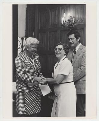 Two unidentified women shake hands as an unidentified man looks on