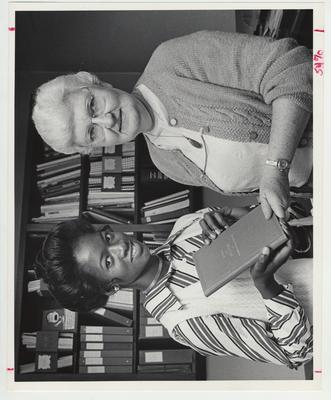 A woman hands a book to an unidentified African - American woman