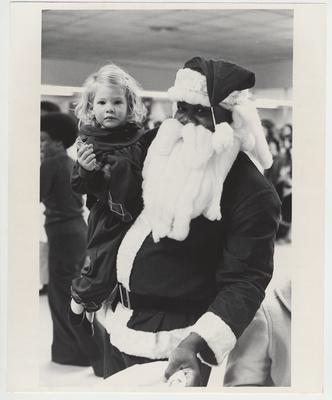 Santa Claus holds a little girl clutching a candy cane