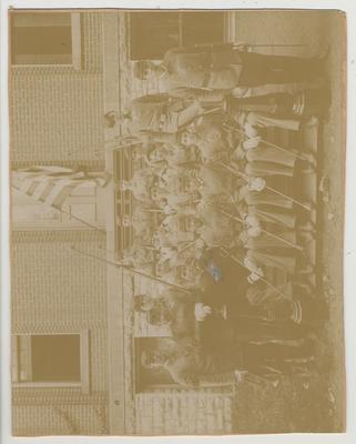 Platoon of men in uniform with sabers and one with a bugle in from of unknown building