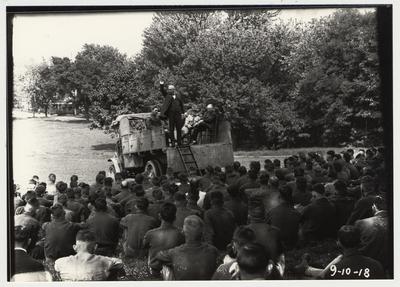 University of Kentucky military training during World War I.  A man giving a speech to several cadets.  F. Paul Anderson is seated in a chair in the back of the truck