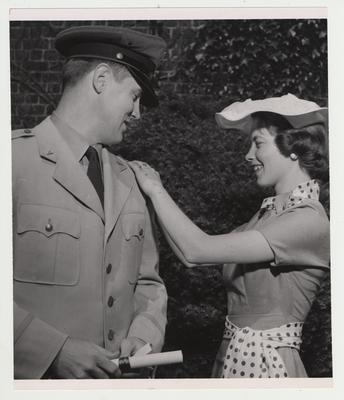 A man in uniform with a woman examining his rank insignia