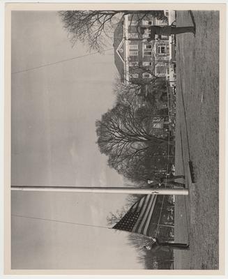 Three men raising the flag in front of the Administration Building with Frazee Hall in the background