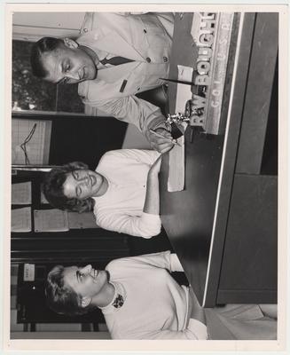 The first female cadets sitting at the Colonel's desk