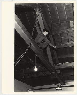 A cadet on top of rafters preparing to possibly rappel to the floor