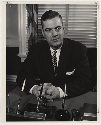 President Frank Dickey seated at his desk with his hands folded together and head slightly turned