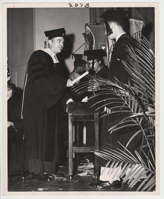 President Frank Dickey (left) in cap and gown presenting a diploma to an unidentified male graduate.  This photo is in the 1957 Kentuckian on page 207, picture number 7