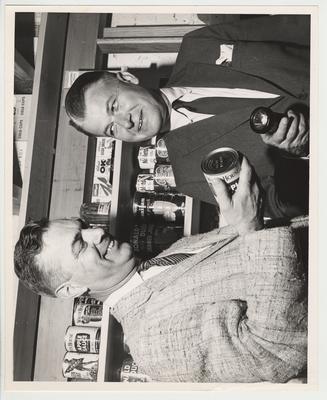 President Frank Dickey (left) and Governor Bert Combs with a flashlight in a model of a bomb shelter with canned goods