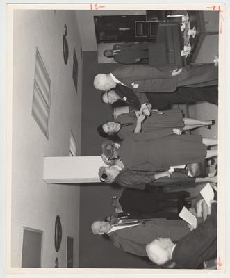 Mrs. Rosanel Oswald (wearing a black hat) is shaking the hand of an unidentified man.  This is located in the Student Center after the appointing of University of Kentucky president John W. Oswald
