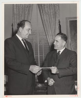 An unidentified man is handing president John Oswald (right) a donation