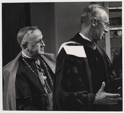 An unidentified Catholic Bishop and an unidentified man prepare for president Oswald's inauguration ceremony
