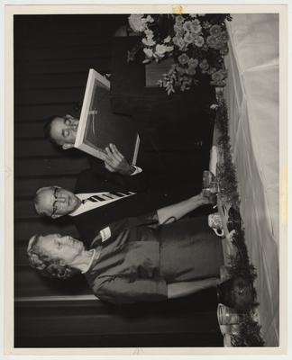 From right to left: President John Oswald (standing at a podium and holding a picture), Mr. Paul Blazer, and Mrs. Georgia Monroe Blazer (a member of the Board of Trustees). Blazer Hall is named after Mrs. Georgia Monroe Blazer