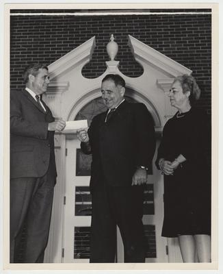 Richard Cooper (far left) handing President John Oswald (center) a check from an unknown donor as Helen King (far right) watches