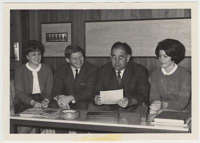 President John Oswald (second from right) seated with three unidentified students, looking at a paper