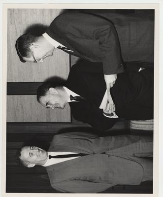 An unidentified man presents a scholarship fund for the University of Kentucky to President John Oswald (center) from the Industrial Community of Blue Grass Centennial Committee