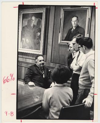 President Oswald (seated) talking to four unidentified students in February 1967.  In the background is a portrait of President Herman Donovan (right) and a portrait of Richard C. Stoll (left)