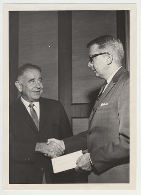 President John Oswald shaking hands with Joseph G. Gibson of Texaco Inc., New Orleans, Louisiana.  Mr. Gibson is holding a check, presumably to be given to the University of Kentucky
