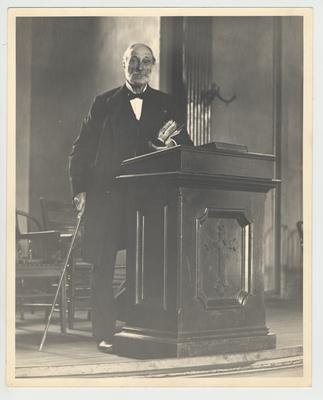 President James Kennedy Patterson standing with a bible behind a podium in a chapel