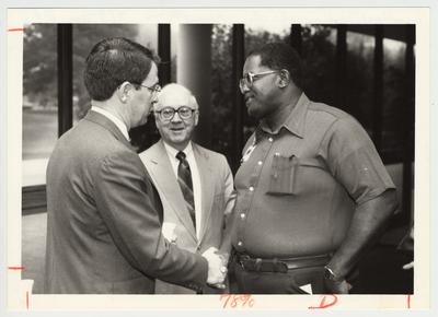 President Roselle (left) is shaking the hand of an unidentified Physical Plant employee at the reception for the Physical Plant Division.  The man in the center is Art Gallaher
