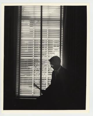 A profile of president Roselle reading a document in front of a window