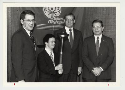 President Roselle (far left) is standing with Scotty Baesler (second from right) Mayor of Lexington.  An unidentified special Olympian (second from left, holding a torch), and an unidentified man (far right) at the Special Olympics ceremony