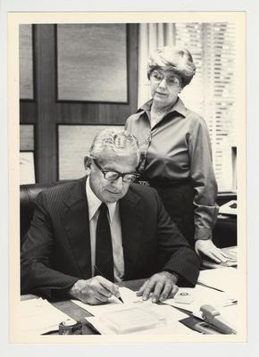 President Singletary signing a document while Evelyn Foster, his secretary, watches