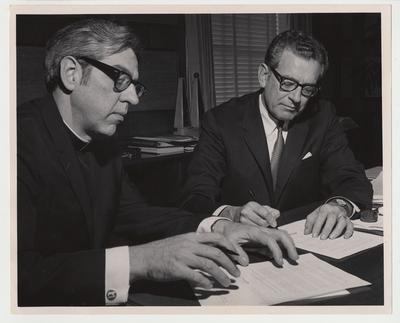 President Singletary (seated, right) is signing an University of Kentucky - Thomas Moore Agreement with an unidentified Catholic priest