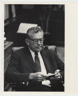 President Singletary seated, reading a book and smoking a pipe