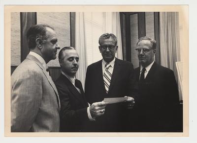 Four men standing together.  From the left:  Unidentified man, Robert McCowan (maybe), President Singletary, and unidentified man.  President Singletary is receiving a check or a document from the man presumed to be Robert McCowan