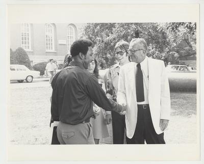 President Singletary is standing outside next to the cannon near the Administration Building.  He is shaking hands with an unidentified male African-American student.  Standing near President Singletary are two unidentified female students and one unidentified male student