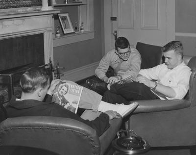 Three unidentified men are looking at magazines in a dorm