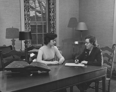 Two unidentified women are seated at a table and talking in a room of Boyd Hall, a woman's dormitory. Boyd Hall was built in 1925 and was named after Cleona Boyd