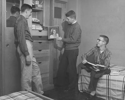 Three unidentified men are looking at a picture of a woman in a Donovan Hall dorm room