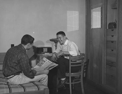 James Thomas (seated in chair) and one unidentified man are socializing in a dorm room of Donovan Hall