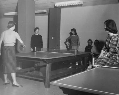 Four unidentified women are watching two unidentified women playing ping pong in Holmes Hall. Photographer: University of Kentucky. Received November 18, 1958 from Public Relations