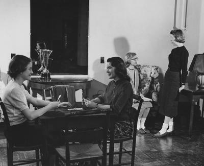 Two unidentified women are playing cards and two unidentified women are talking in Jewell Hall. Jewell Hall was named after Mary Frances Jewell. Received March 16, 1957 from Public Relations