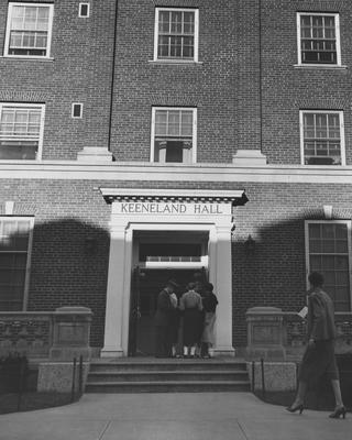 Unidentified people standing on the front steps to Keeneland Hall, a woman's dormitory. Keeneland Hall was named after the Keeneland Foundation which donated $200,000 and on October 17, 1955, it was dedicated to the foundation. Received March 16, 1957 from Public Relations