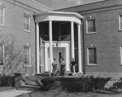 Nancy Taylor (front row, left), Patricia Vry (front row, right), and two unidentified women are standing in front of the Alpha Delta Pi House. This photo is on page 59 of the 1956-1957 