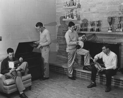 Two unidentified men are cleaning trophies, one unidentified man is reading and one unidentified man is playing a record in the Recreation room of the Kappa Sigma house. Received March 18, 1957 from Public Relations