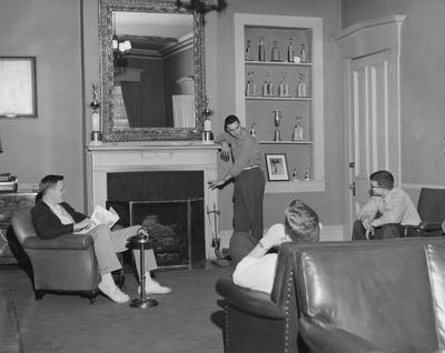 Four unidentified men are conversing in the living room of the Sigma Alpha Epsilon house. Received August 7, 1957 from Public Relations