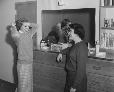 Sarah Jarrett Hodges of Pikeville, Kentucky (left, wearing a plaid skirt) and an unidentified woman are conversing in a bed room of the Kappa Alpha Theta house. Received January 16, 1959 from Public Relations
