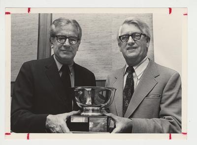 President Singletary (left) is standing and holding an award with David Blythe (right).  The award was given to the University of Kentucky for providing the most overall support for the United Way of the Bluegrass' 1975 - 1976 campaign