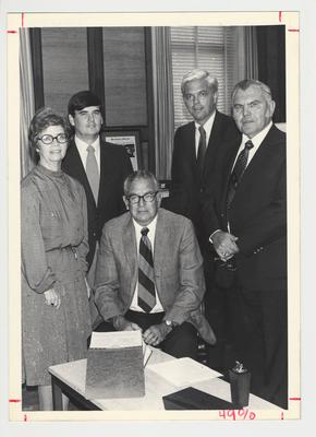 Three unidentified men and one unidentified woman are at the signing of a document by President Singletary (seated)