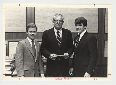 Two unidentified men are either presenting a check to or are receiving a check from President Otis Singletary (center)