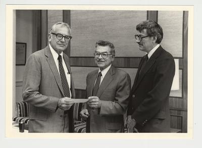 Two unidentified men are either presenting a check to or are receiving a check from President Otis Singletary (center)