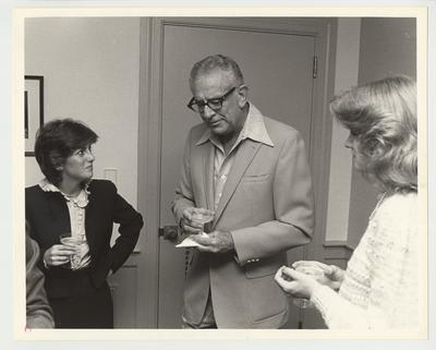 President Singletary (center) is standing and having a drink with two unidentified women at the surprise birthday party thrown by the Mortar Board
