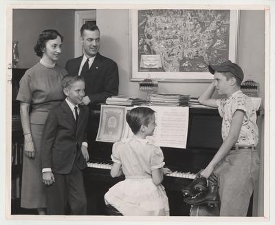 President and Mrs. Frank G. Dickey and their children relax at home.  They are gathered around the piano while one of the children plays