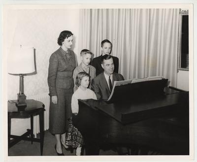 From the left:  Betty (standing); Joe (standing); Frank Dickey Jr. (standing); Ann (sitting); and President Dickey (seated).  The family is gathered around a piano.  Received by Public Relations on August 17, 1957