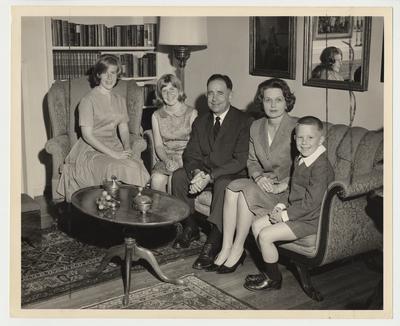 The Oswald Family are seated together in a living room.  From the left:  Nancy, Elizabeth, President Oswald, his wife Rosanel, and Johnny