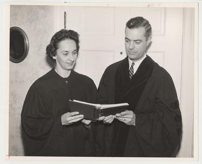 Betty Dickey (left) is standing with her husband Frank Dickey (right).  She is holding a book and is dressed a robe